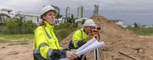 Survey team reviewing plans while using leveling equipment at an active construction site, representing the work of Southpoint Geodetics land surveyor