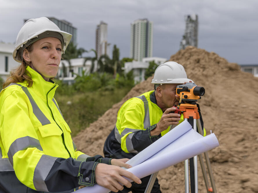 Survey team reviewing plans while using leveling equipment at an active construction site, representing the work of Southpoint Geodetics land surveyor