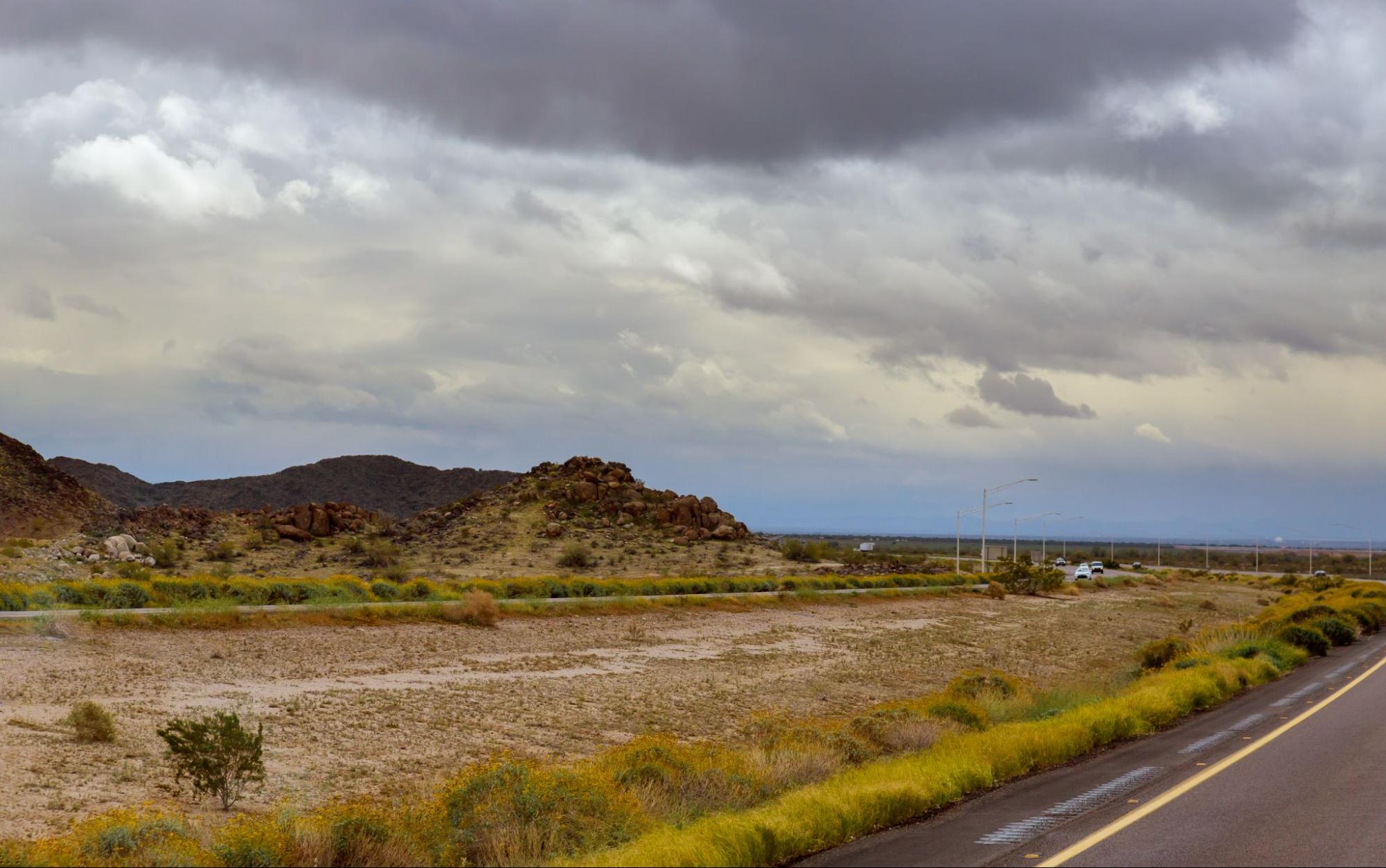 South Texas land with desert terrain, roadside view, rocky hills, and cloudy sky over wide open rural landscape