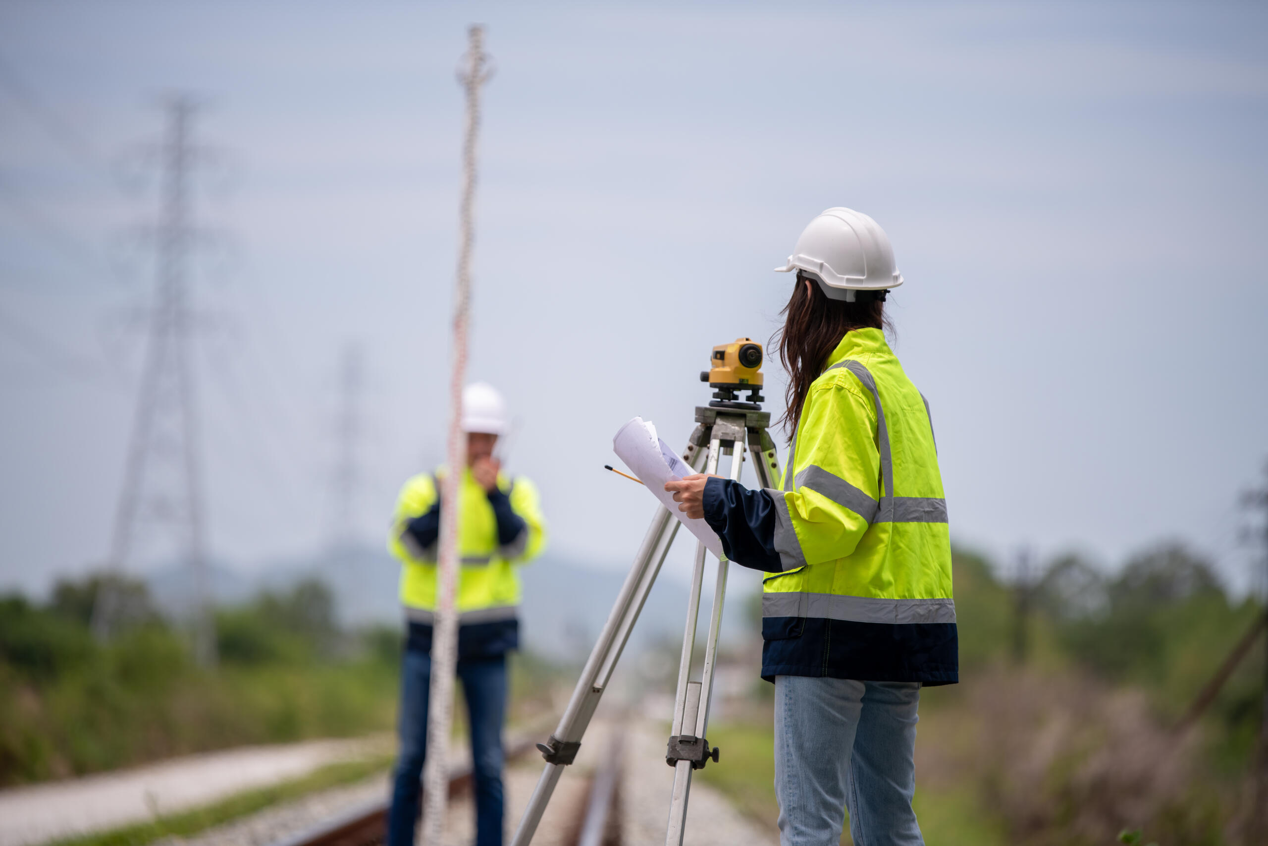 Survey team using leveling equipment and grade rod along railway tracks for land measurement work.