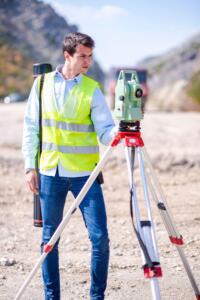 Engineer using tripod survey equipment on a roadside job site