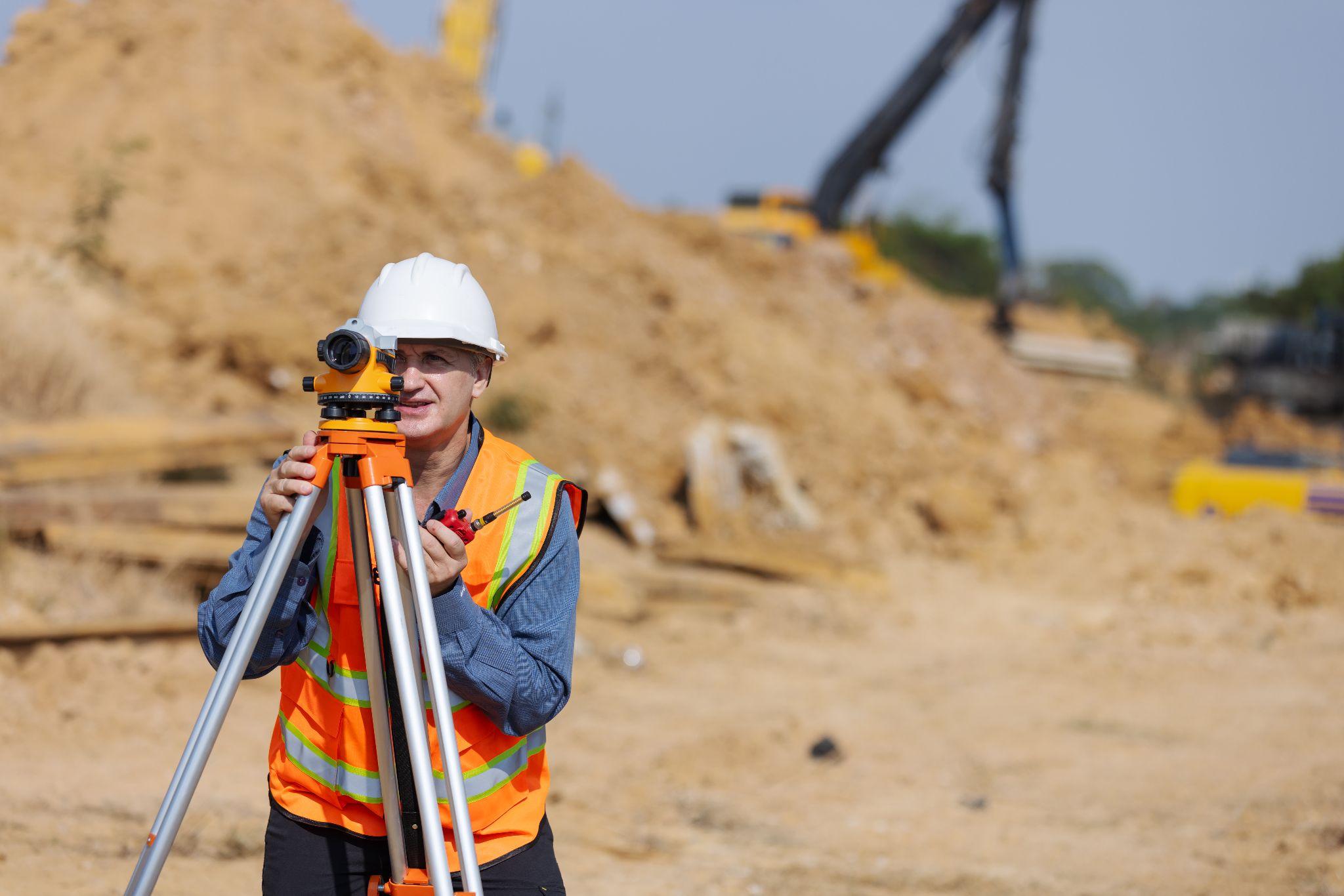 Construction surveyor operating a level instrument at an excavation site where teams book a land surveyor before building begins.
