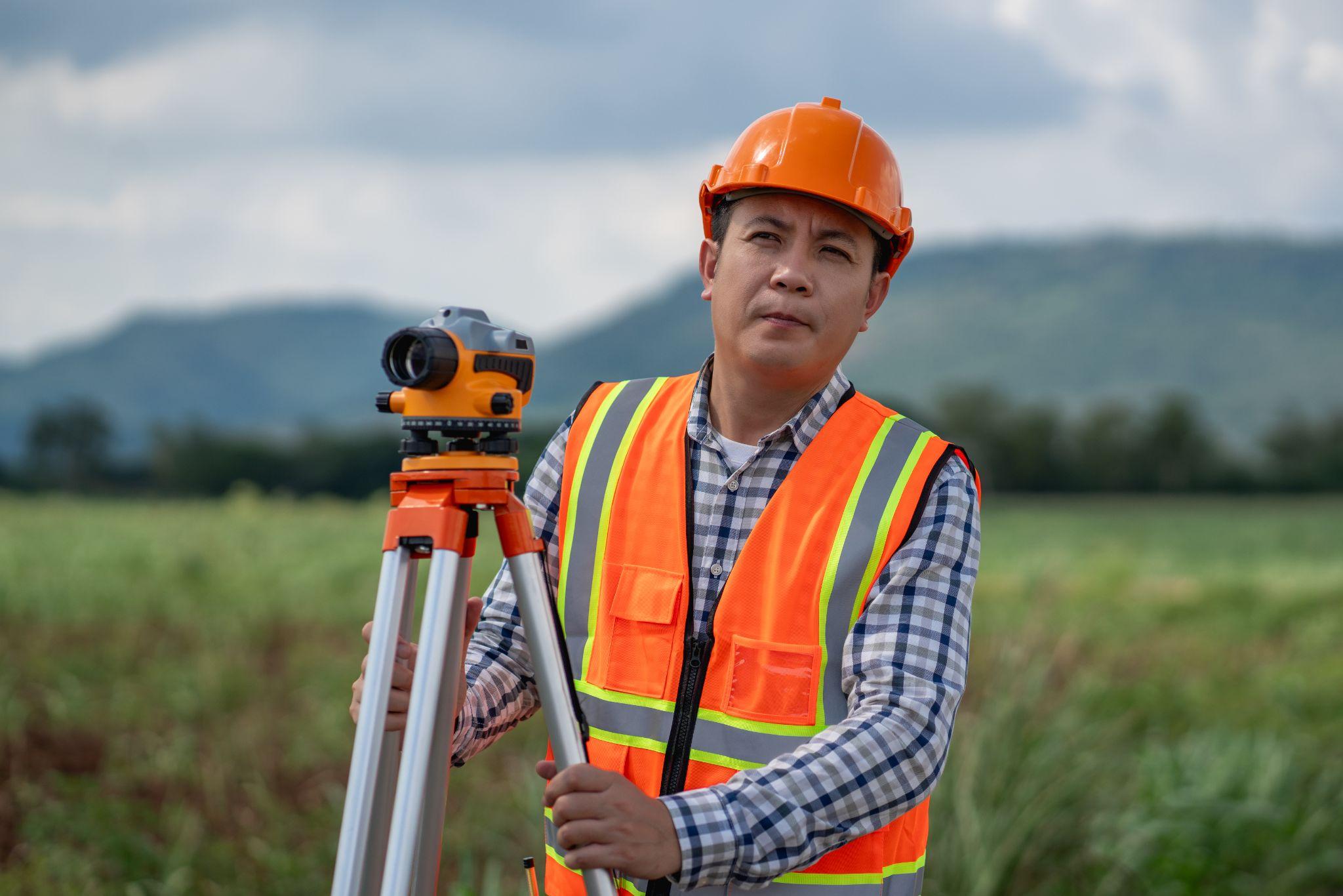Field surveyor with tripod equipment in open land showing why developers should book a land surveyor early.