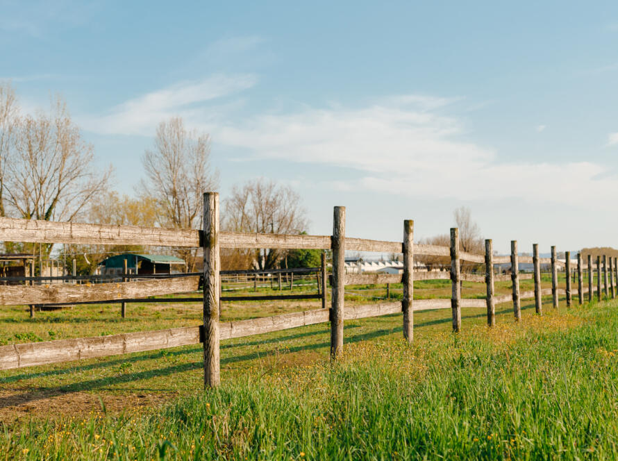 An old wood fence with a green country field behind it, representing the need to contact a professional land surveyor