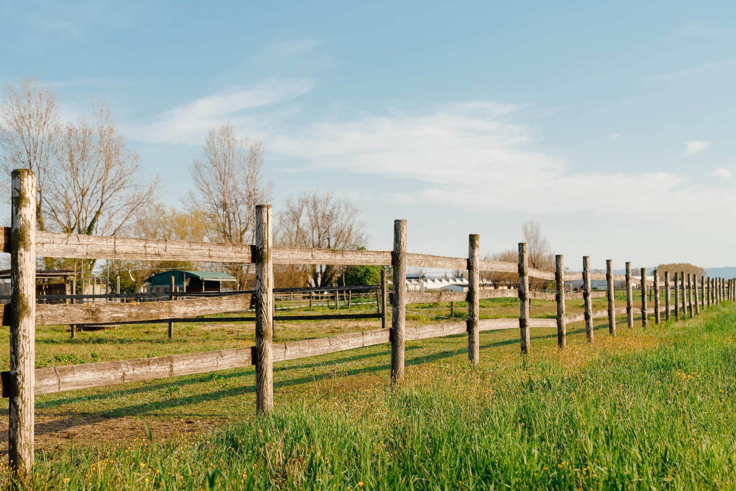 An old wood fence with a green country field behind it, representing the need to contact a professional land surveyor