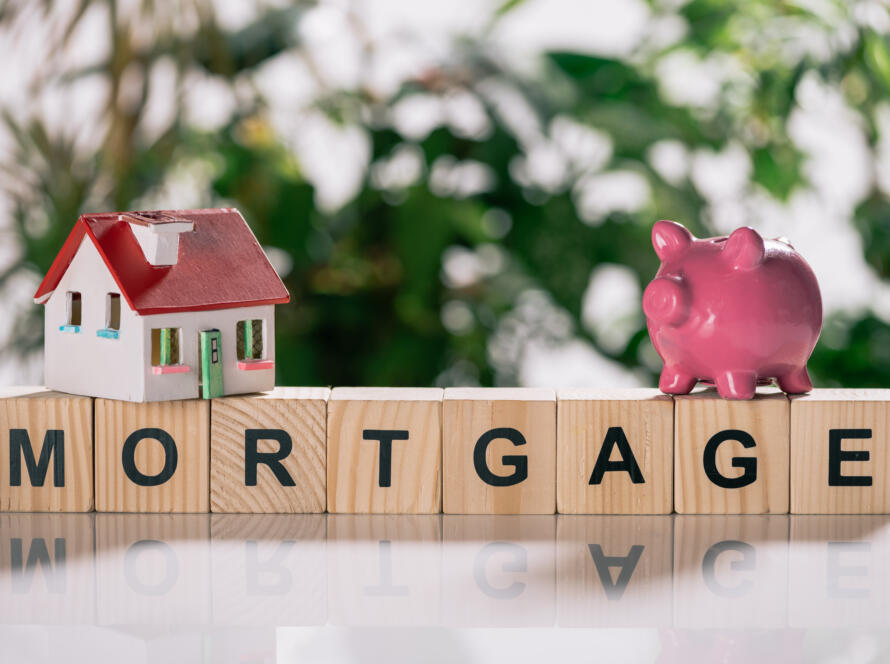 selective focus of house model and piggy bank on wooden cubes with letters, mortgage concept representing the need for a land surveyor for mortgage closing