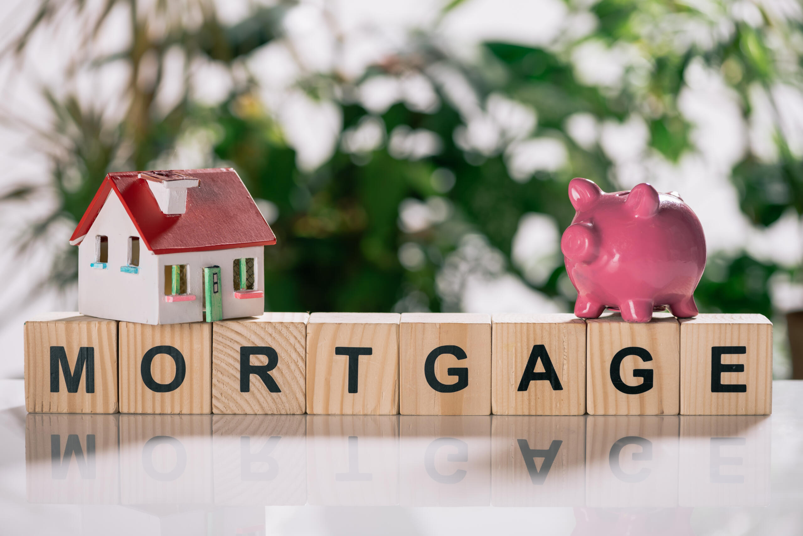 selective focus of house model and piggy bank on wooden cubes with letters, mortgage concept representing the need for a land surveyor for mortgage closing