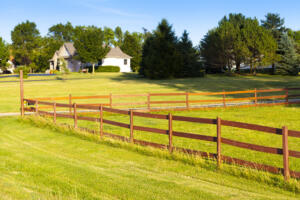 A wooden property line fence enclosing a lush green suburban lawn and residential home, illustrating the need for a professional land survey services for real estate transactions before closing.