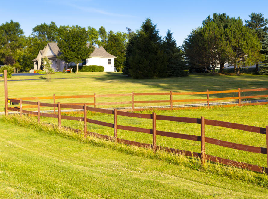 A wooden property line fence enclosing a lush green suburban lawn and residential home, illustrating the need for a professional land survey services for real estate transactions before closing.