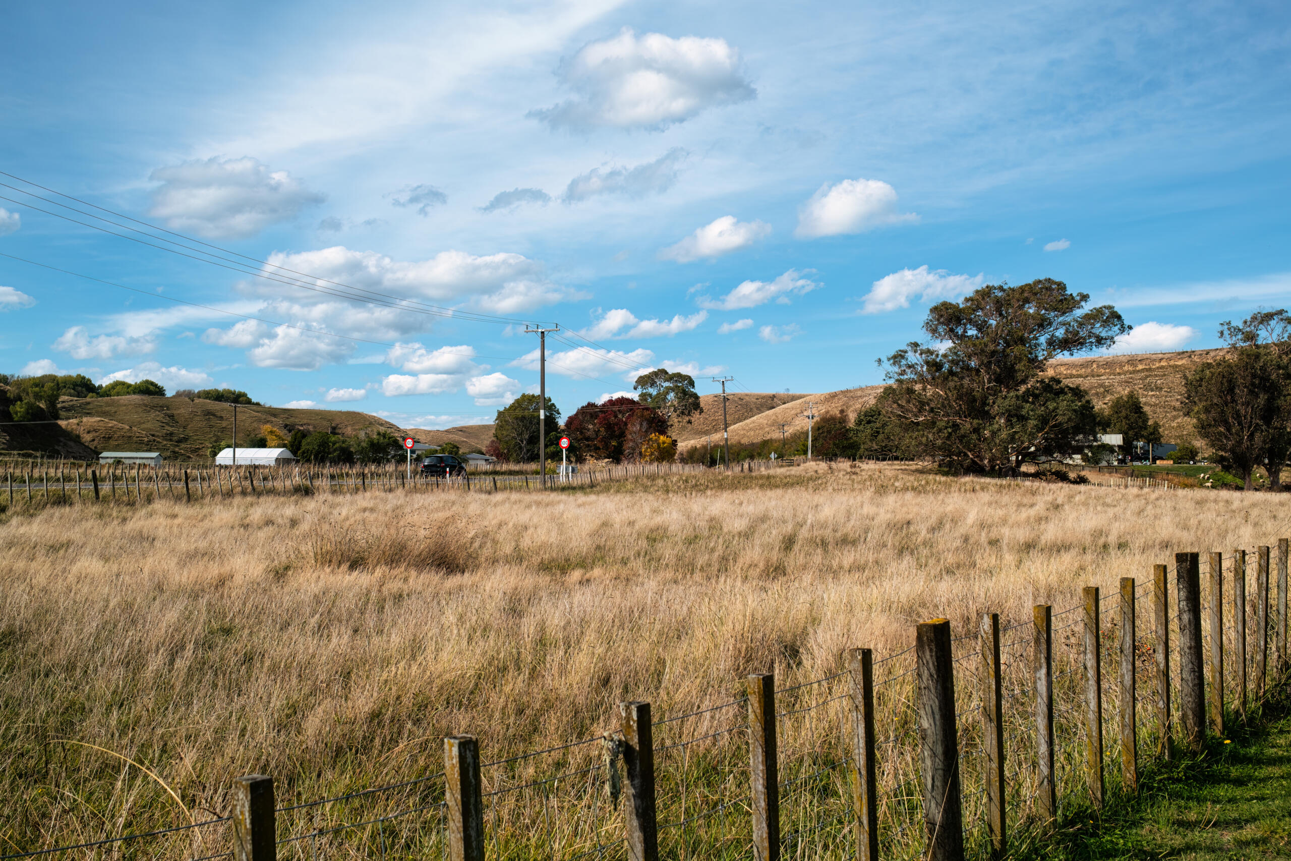 Rural grassy field bounded by a wooden post fence, showing power poles and a road in the distance, illustrating where professional land survey services for real estate transactions evaluate property boundaries.