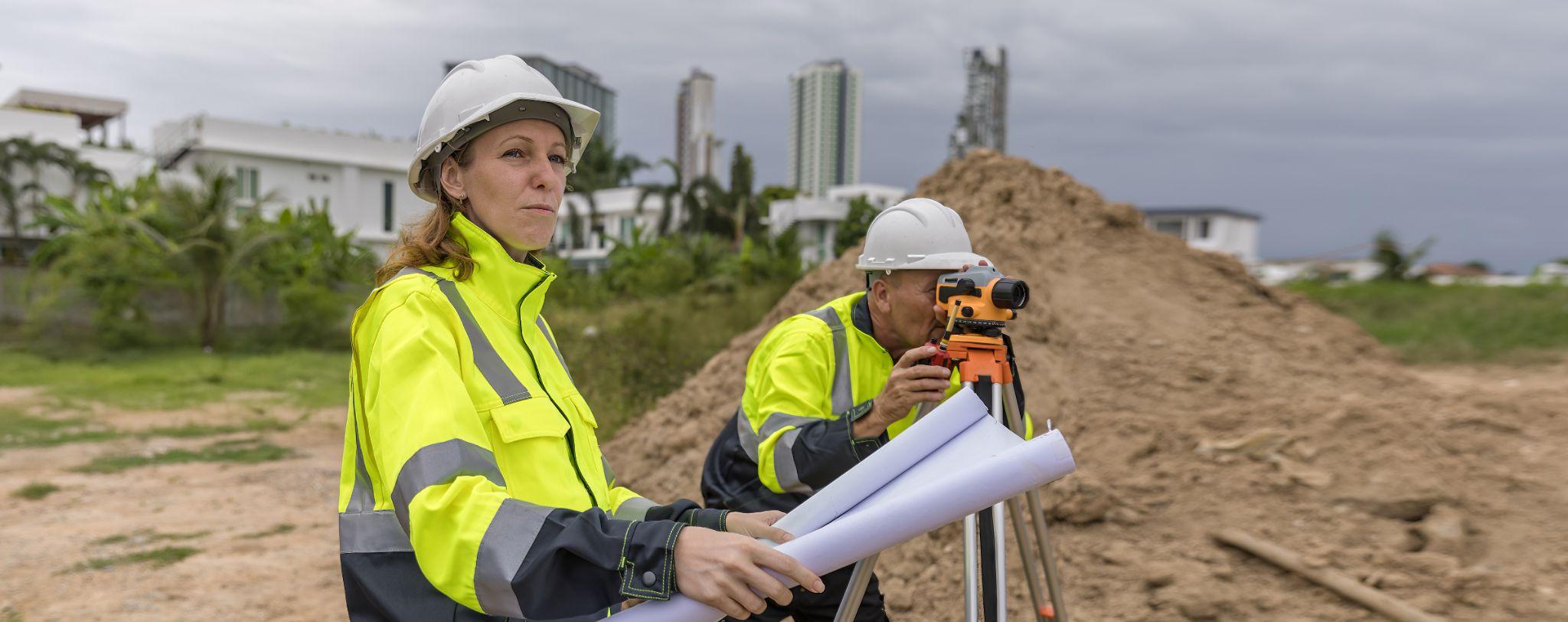 Surveyors using field equipment and reviewing plans for a commercial land surveying quote at a construction site.