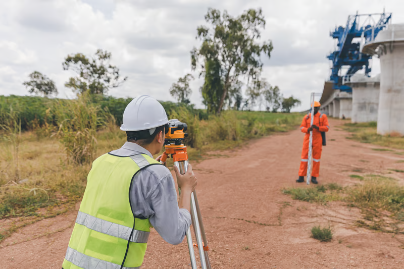 Land surveyor using professional equipment at a construction site, illustrating a licensed land surveyor contact for property projects.