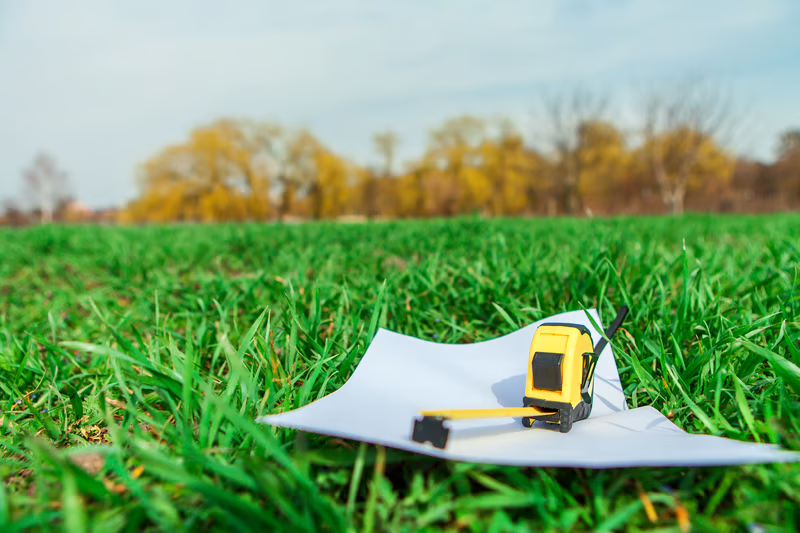 Survey plans and measuring tape placed on open land, representing property preparation before contacting a licensed land surveyor.