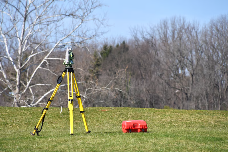 Surveying equipment set up on an open property for field measurements used to prepare a topographic survey estimate.