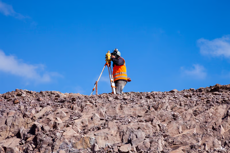Land surveyor using a total station to measure elevations on rocky terrain