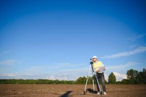 Land surveyor using a total station to measure property boundaries on an open tract of land