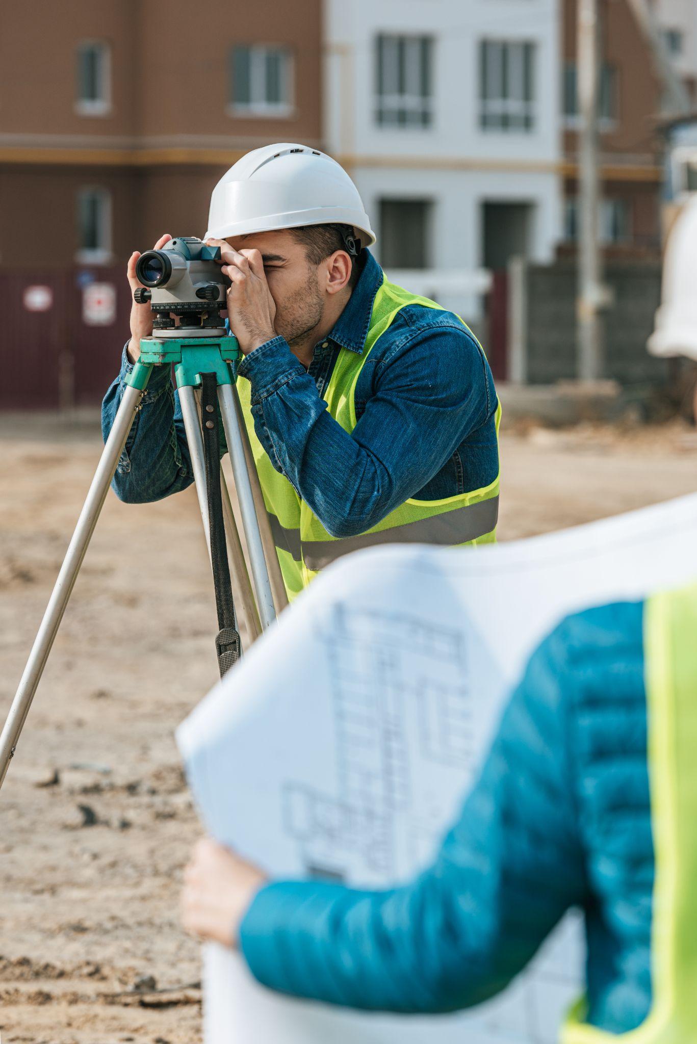 Land surveyor using field equipment and plans at a construction site