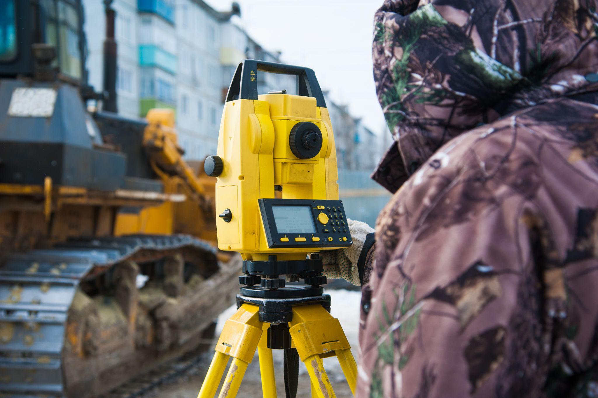 Surveyor using measuring equipment at an active construction site
